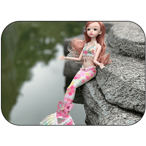 Colorful mermaid doll sitting on rocks near water, perfect for creative play and imaginative adventures, ideal for holiday gift shopping.